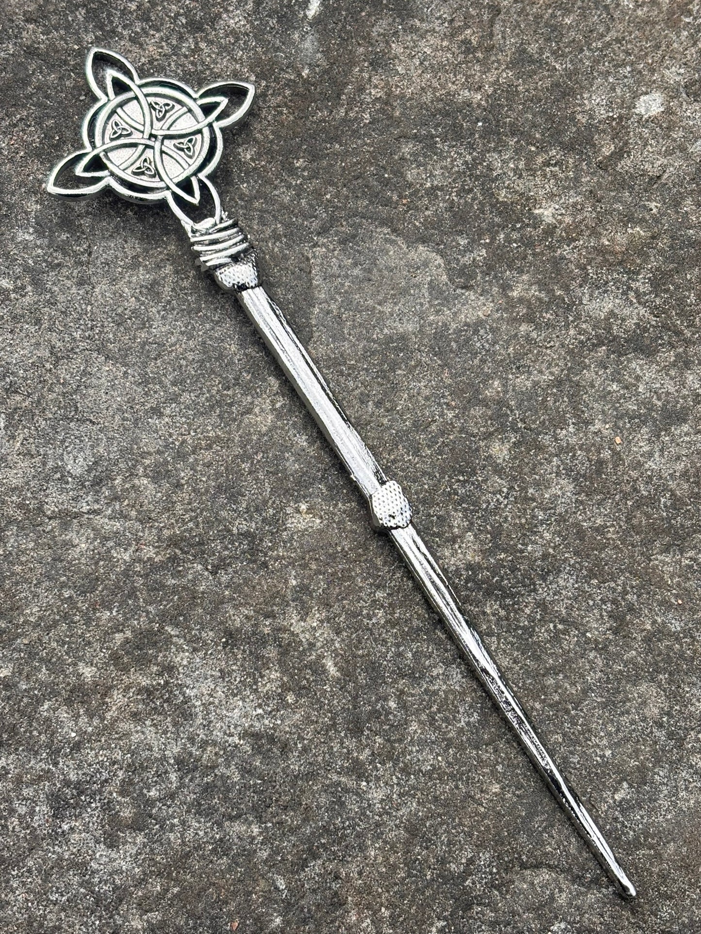 A Celtic Cross Hair Pin — Antique Silver with an ornate Celtic knotwork and triple-circle emblem on the top, resting diagonally on a textured gray stone surface.