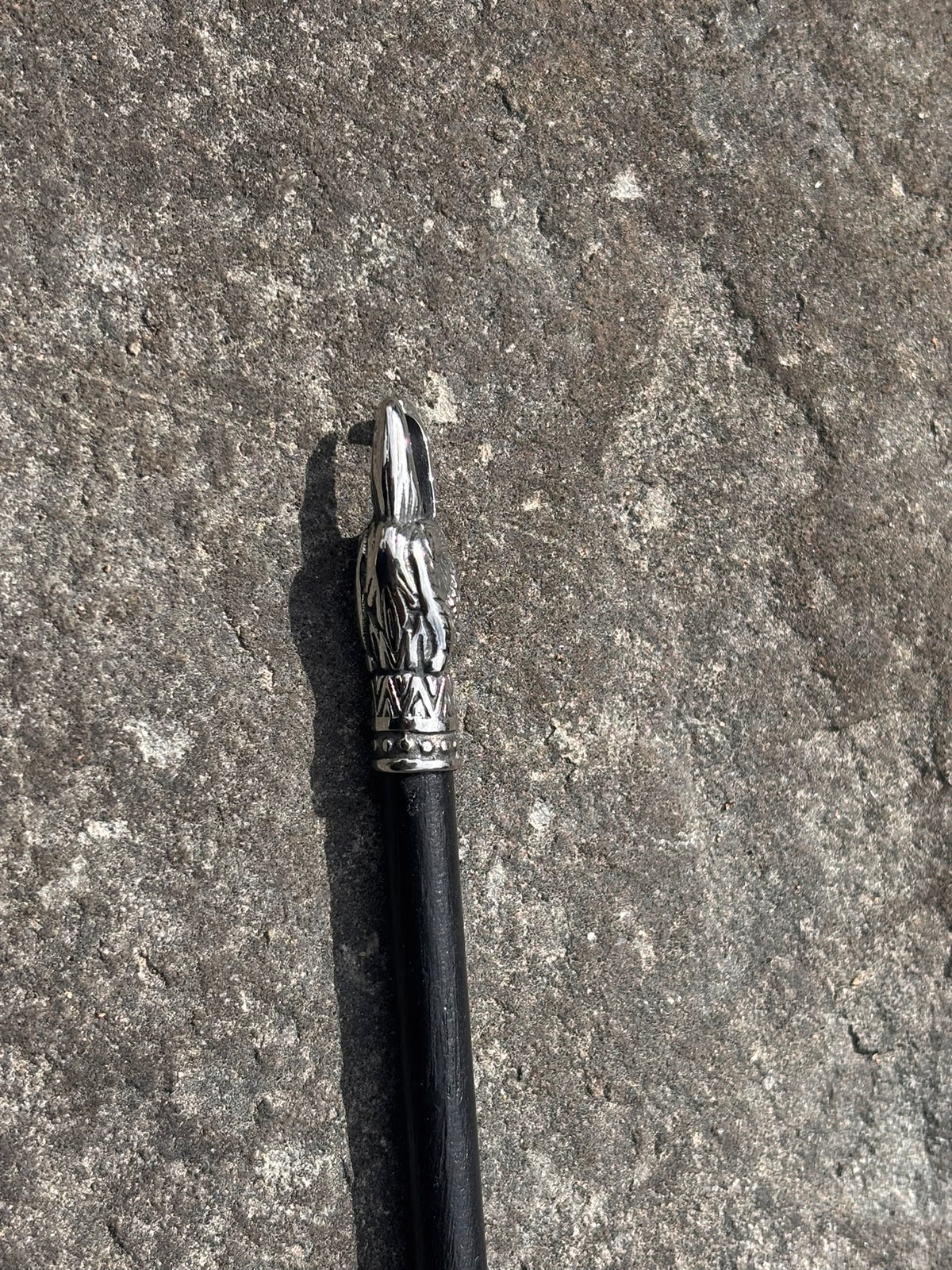 A black-handled hair pin with an ornate silver eagle head metal cap featuring a sculpted animal head, photographed on a rough gray stone surface.
