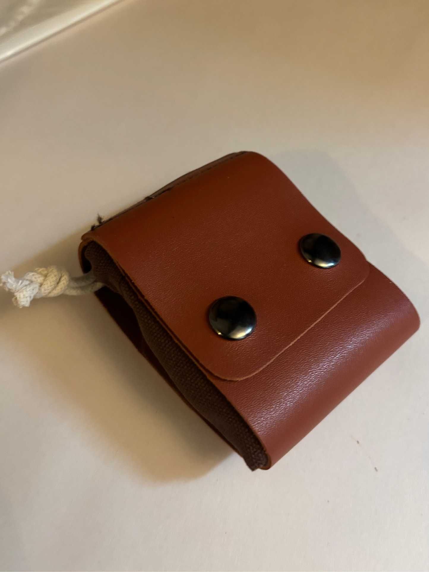Brown leather clip for connecting foraging bag to a belt with two silver buttons on a white surface