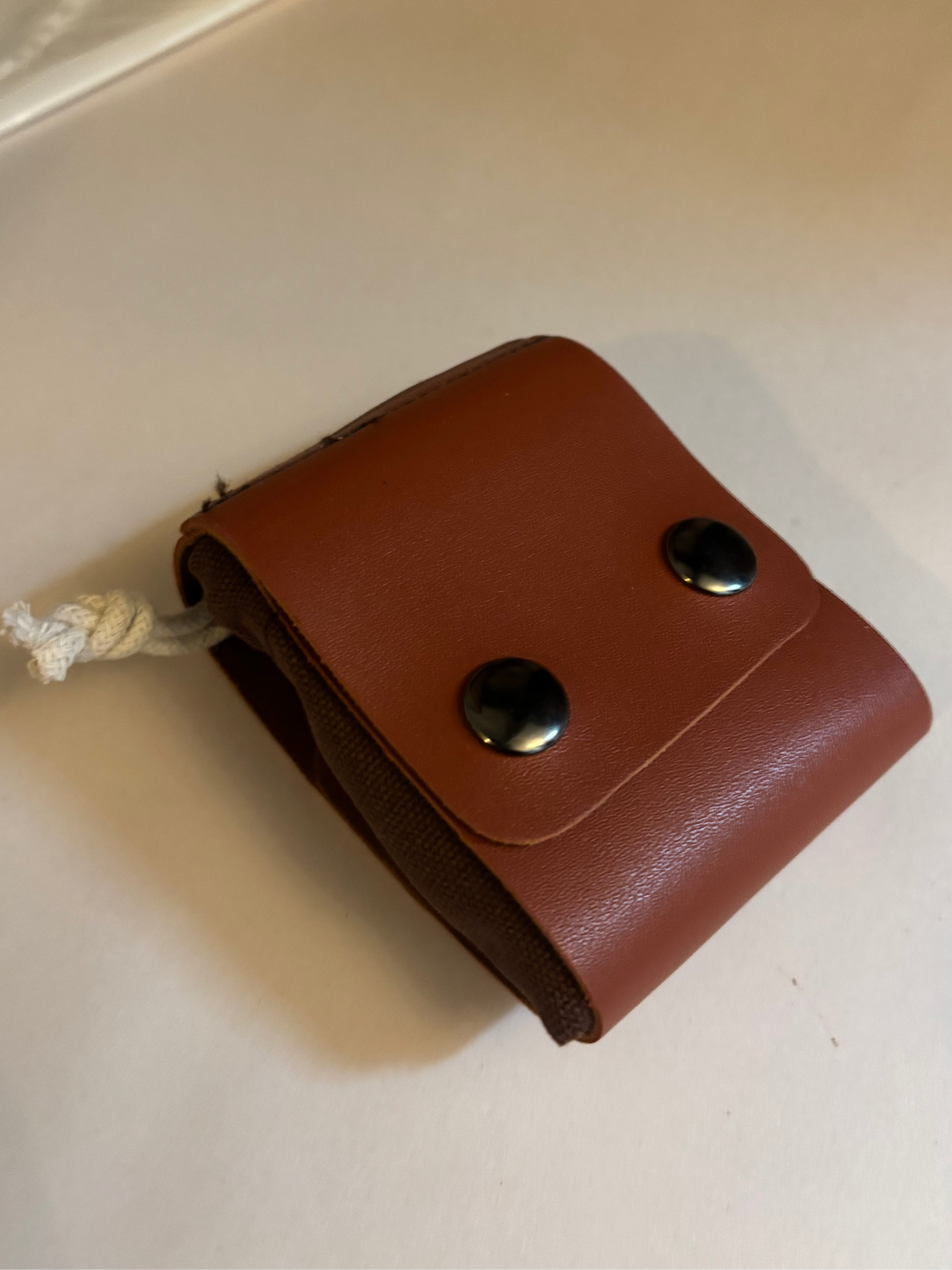 Brown leather clip for connecting foraging bag to a belt with two silver buttons on a white surface