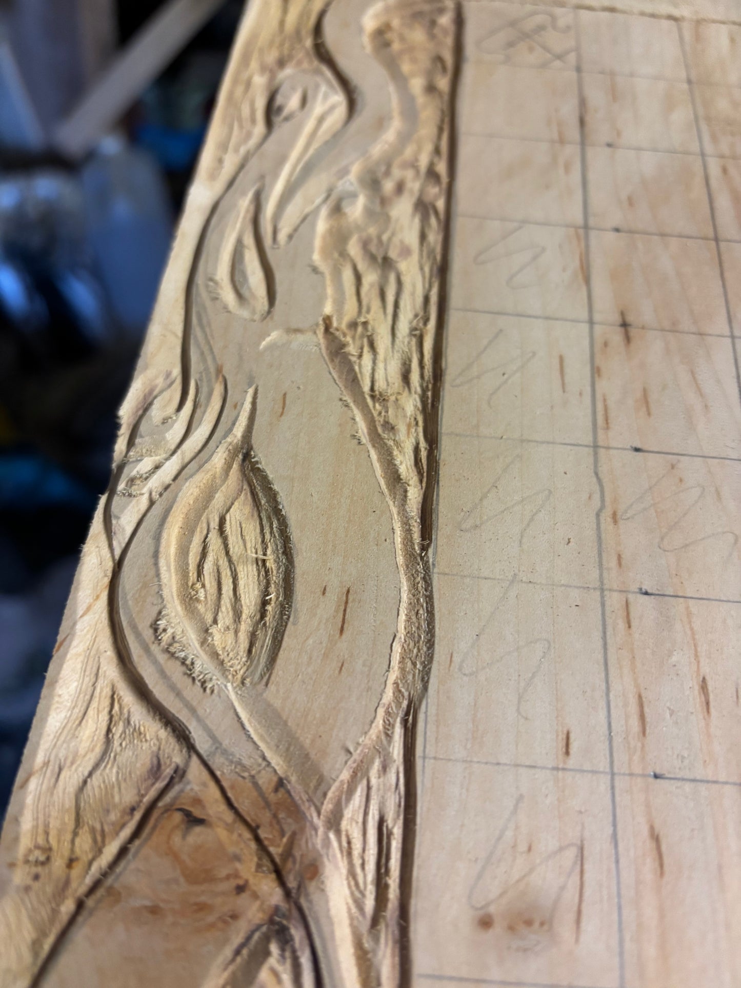 Close-up of a carved wooden panel with a natural leaf-like relief design on the left, next to a lighter wood surface marked with faint grid lines.