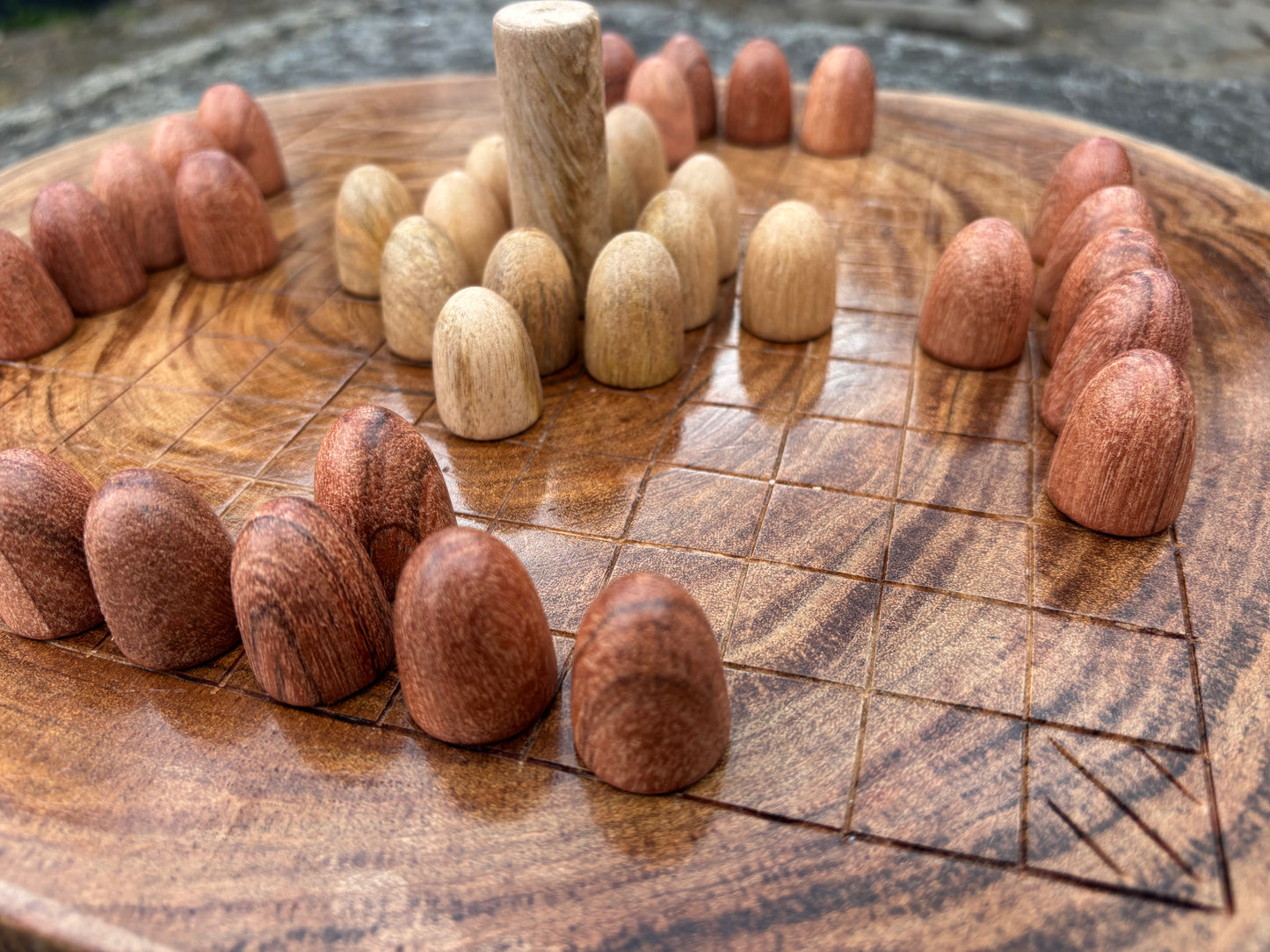 Hnefatafl Set — Plain Wood. A close-up of a round wooden board game with small wooden pieces arranged in a circular formation on a carved wooden board.
