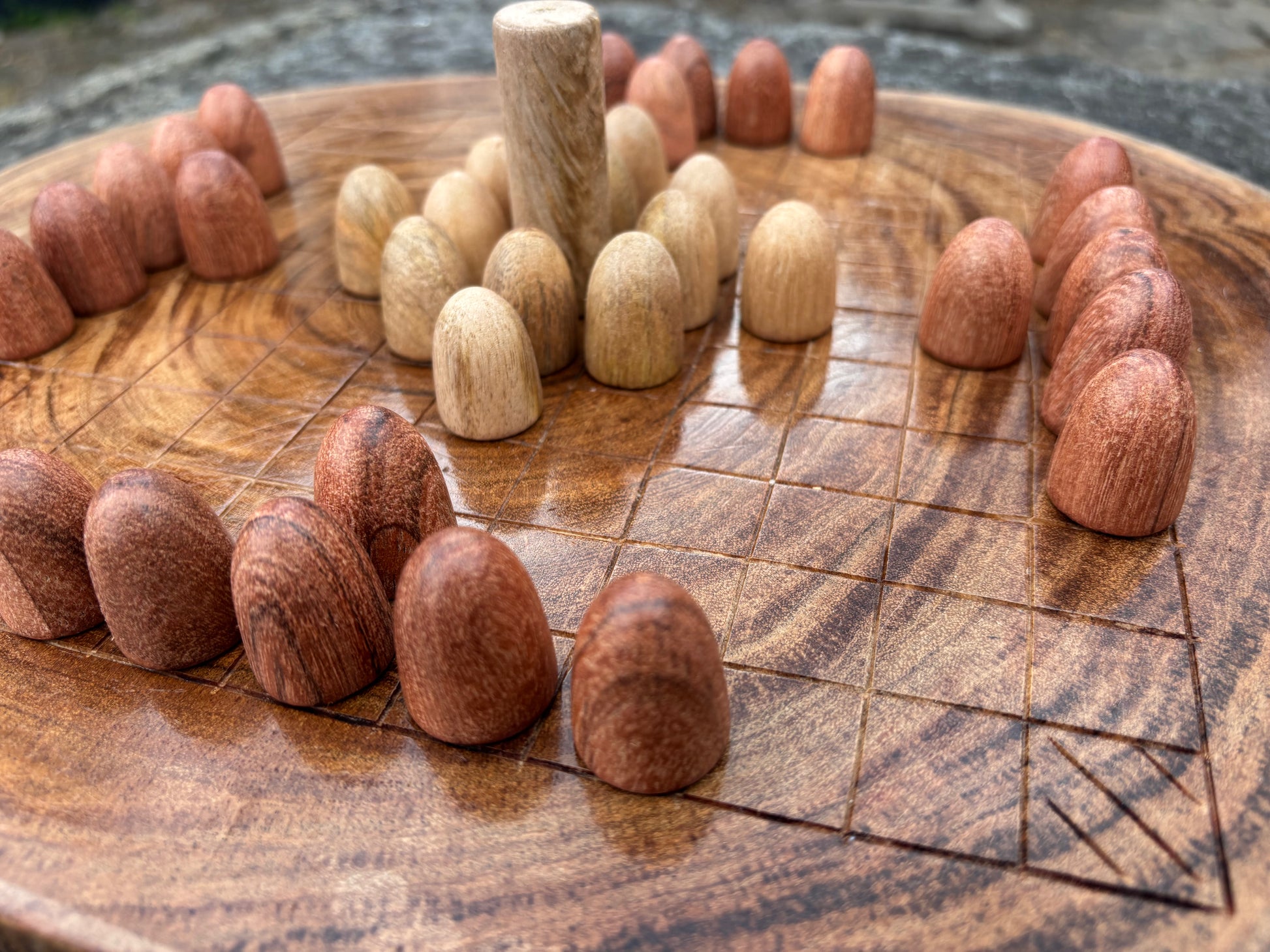 Hnefatafl Set — Plain Wood. A close-up of a round wooden board game with small wooden pieces arranged in a circular formation on a carved wooden board.