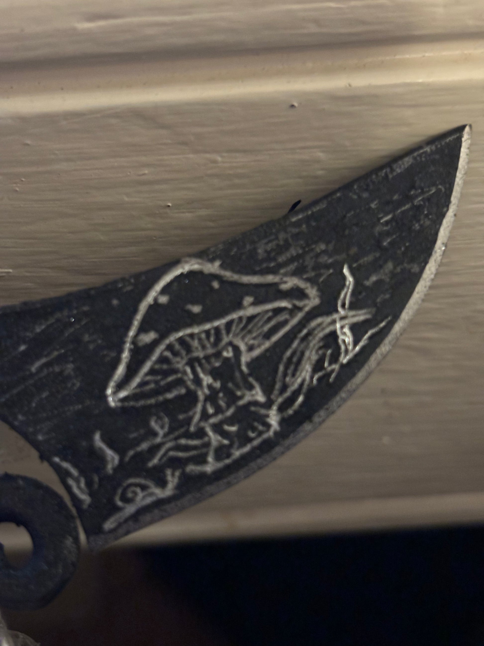 Black knife blade with white etched mushroom and plant design against a beige background.