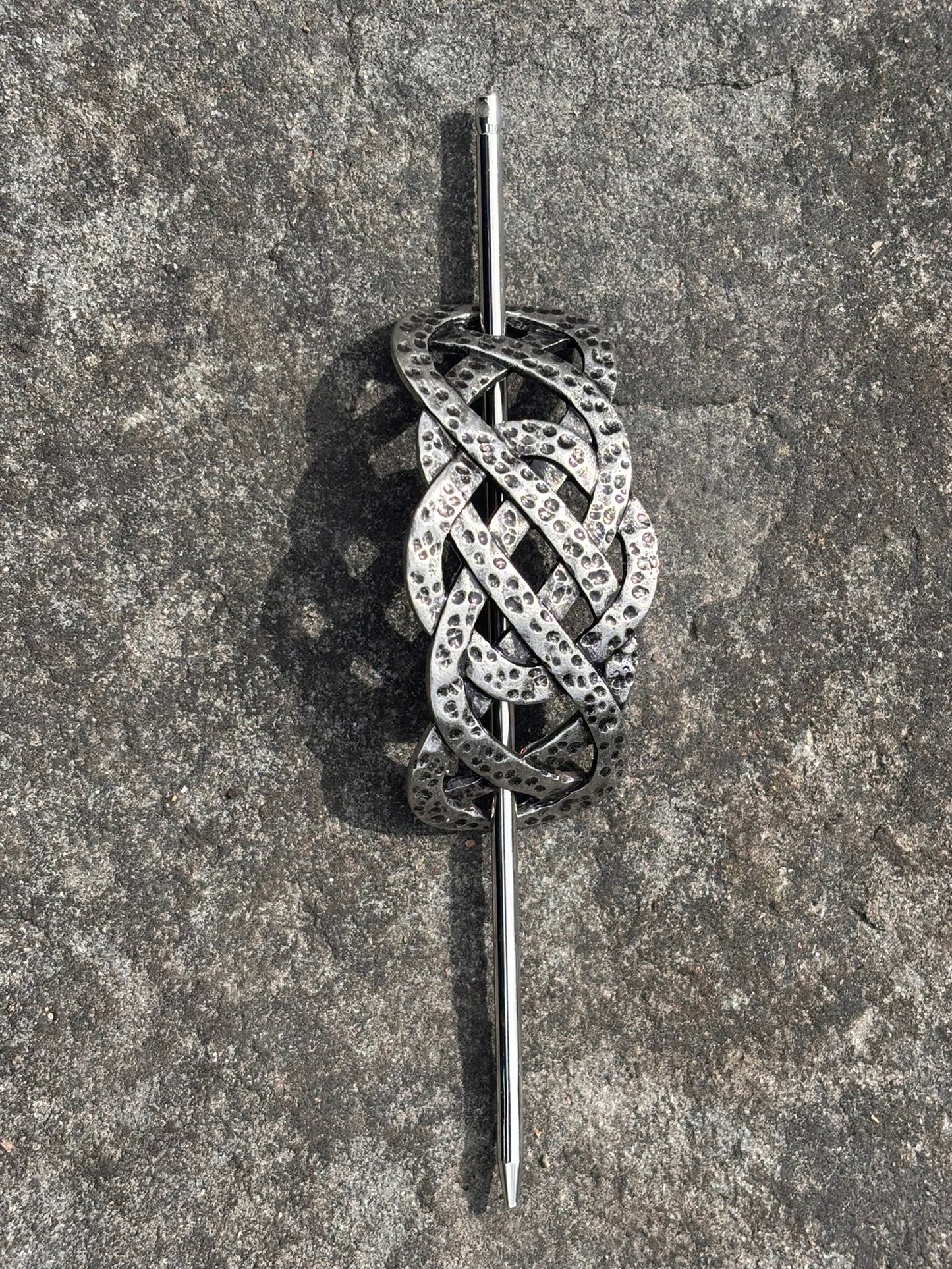 Nordic Celtic Knot Hair Slide — Antique Silver featuring an intricate, interwoven Celtic knot design with small clear stones, mounted on a straight pin, displayed on a textured gray stone surface.