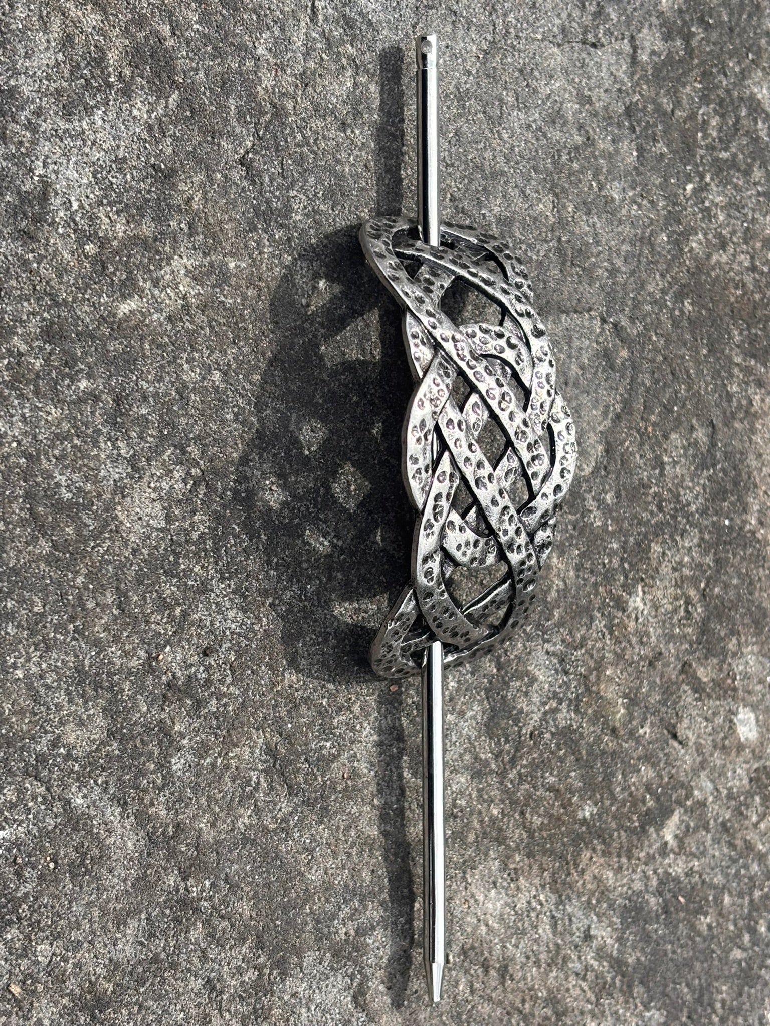 A silver-Nordic Celtic knot hair slide with a pin bar, displayed on a textured gray stone surface.