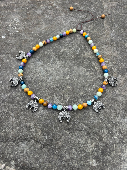 A beaded necklace with colorful round beads in yellow, orange, blue, purple, and white, accented by five silver-toned elephant charms, displayed on a textured gray stone surface. Viking lunula necklace