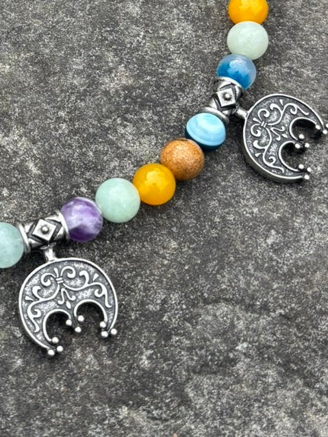 The Moon Maiden's Cord — Viking Lunula & Stone Bead Necklace with colorful round beads and five silver crescent moon charms, displayed on a textured gray stone surface.
