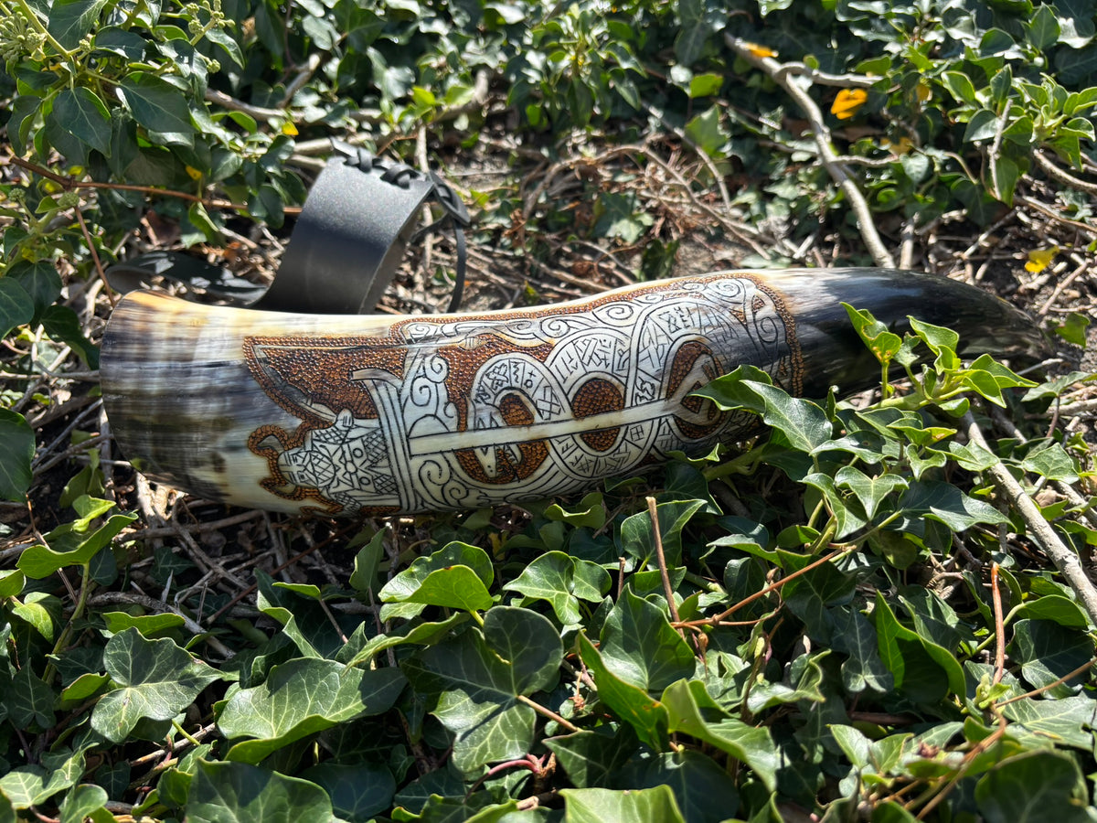 An engraved horn with intricate Celtic-style knotwork and animal motifs, resting on green ivy and branches outdoors.