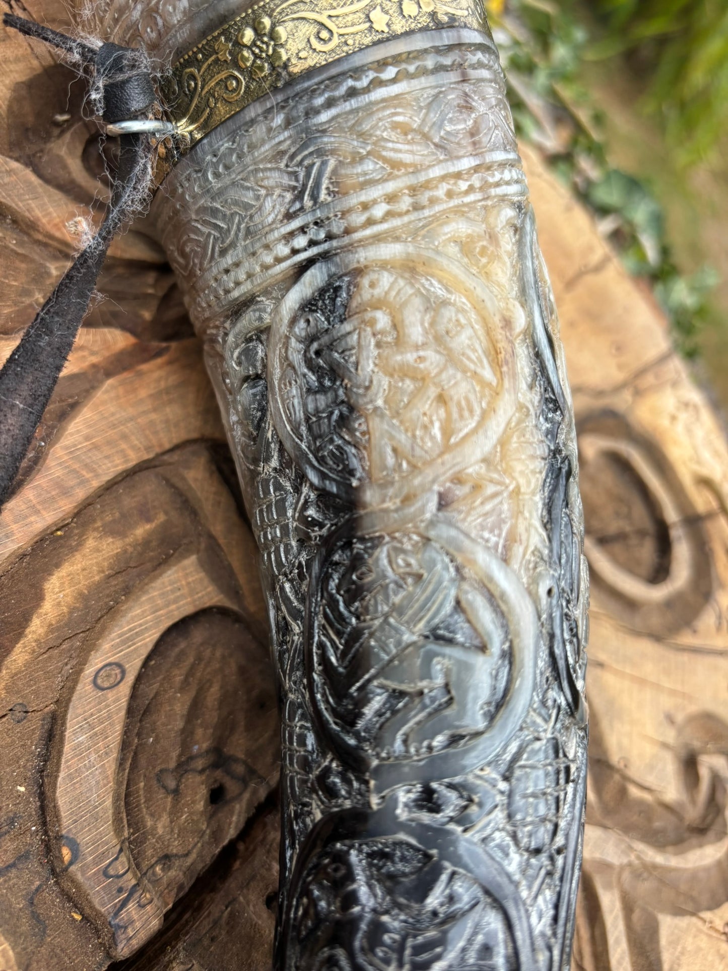 An ornate carved horn or antler-style accessory with intricate embossed animal and geometric patterns, shown close up on a carved wooden surface.