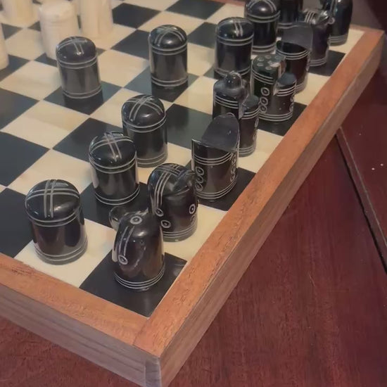 Close-up of a wooden chessboard with black and white pieces set up on a polished table.
